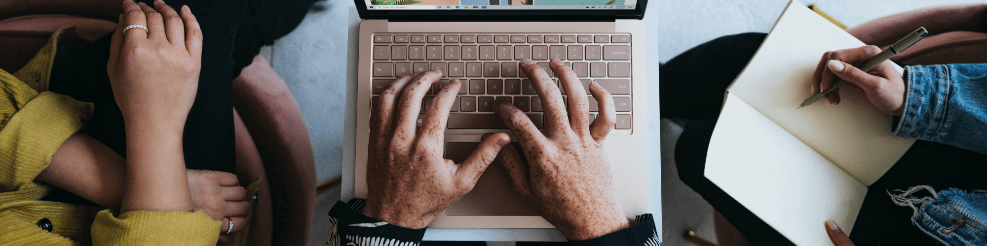 aerial image of close up of three people's hands working on a laptop and a notebook. collaborative workplace