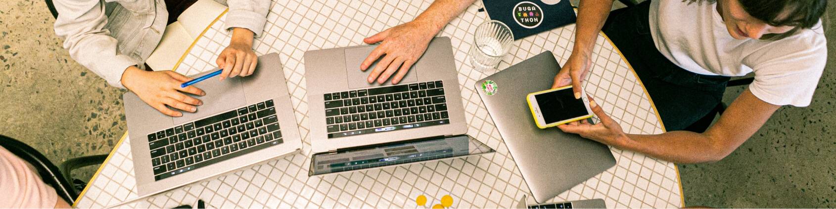 view from above of a table with three laptops and the hands of people working together