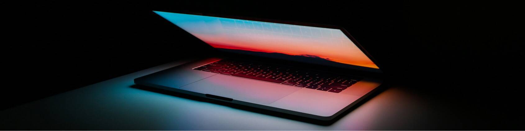 Half closed laptop sits on a table in a dark room. The computer glows with a red screen.