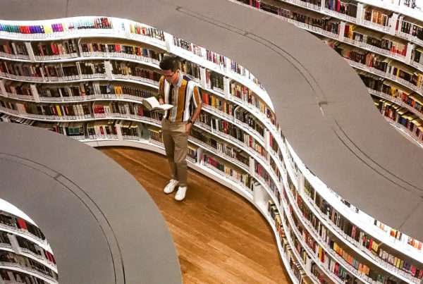 man stands between the stacks in a modern libary with curved bookshelves