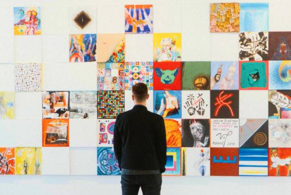 man stands looking at a wall of brightly coloured square canvas paintings