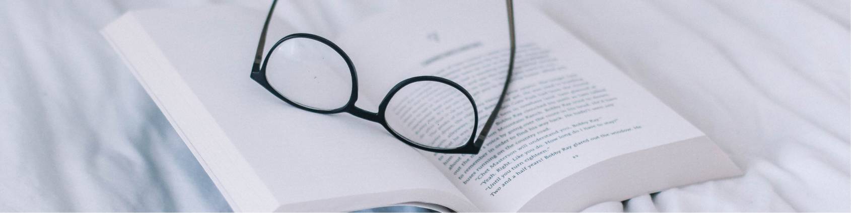 open paperback book on a bed with eye glasses holding the page open